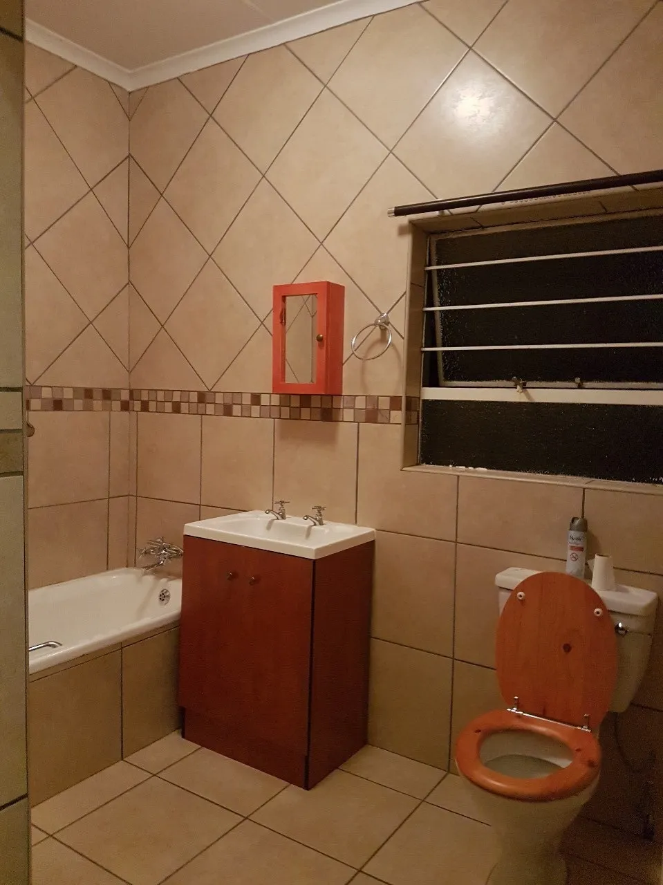 The same bathroom before: beige tiles, a timber vanity and an orange toilet seat.