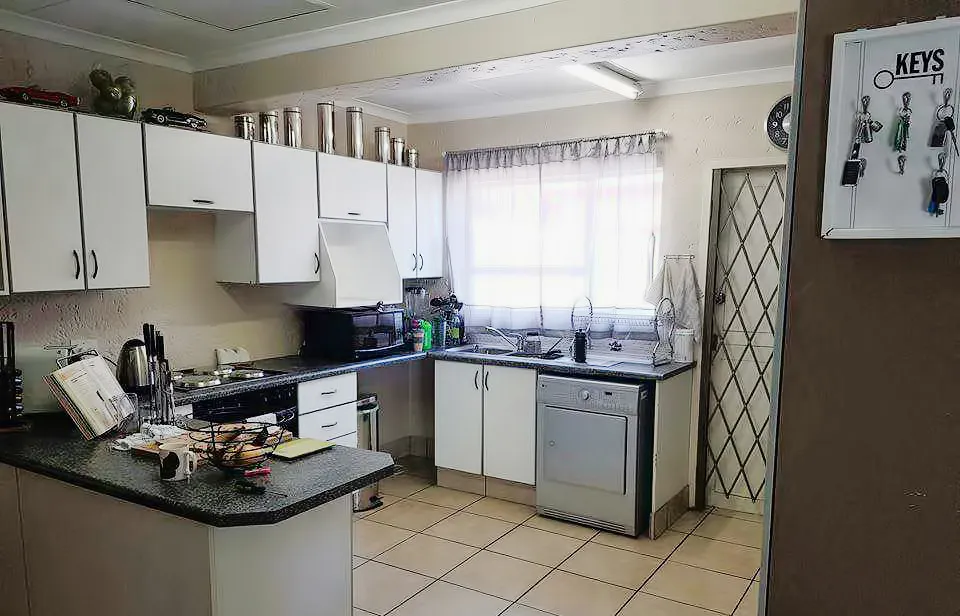 Before: a kitchen with white cabinets, dark speckled countertops and a tiled floor, with a key holder on the wall in the foreground.