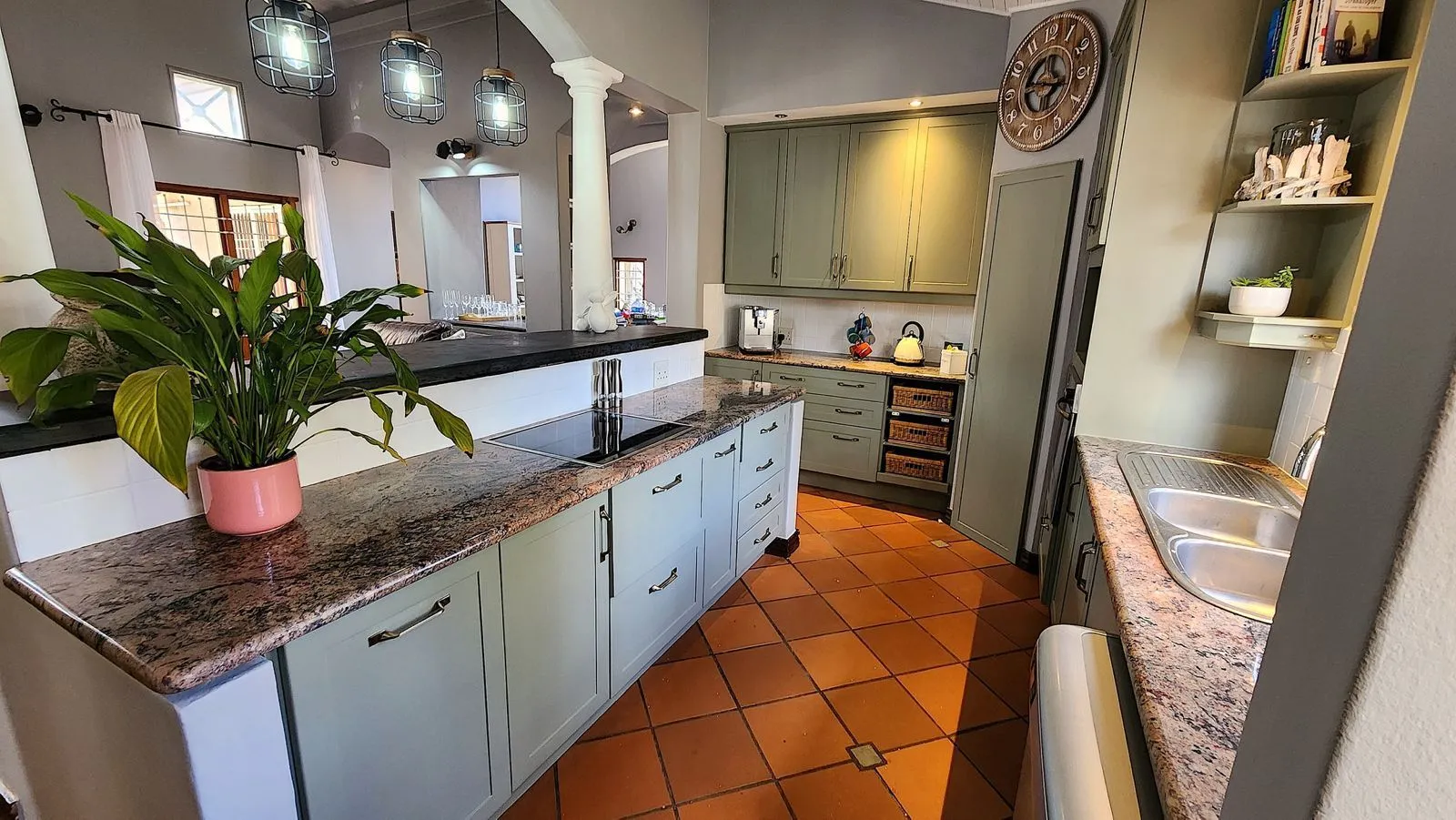 After: the same kitchen with sage green cabinets, the granite island and a peace lily in a pink pot.