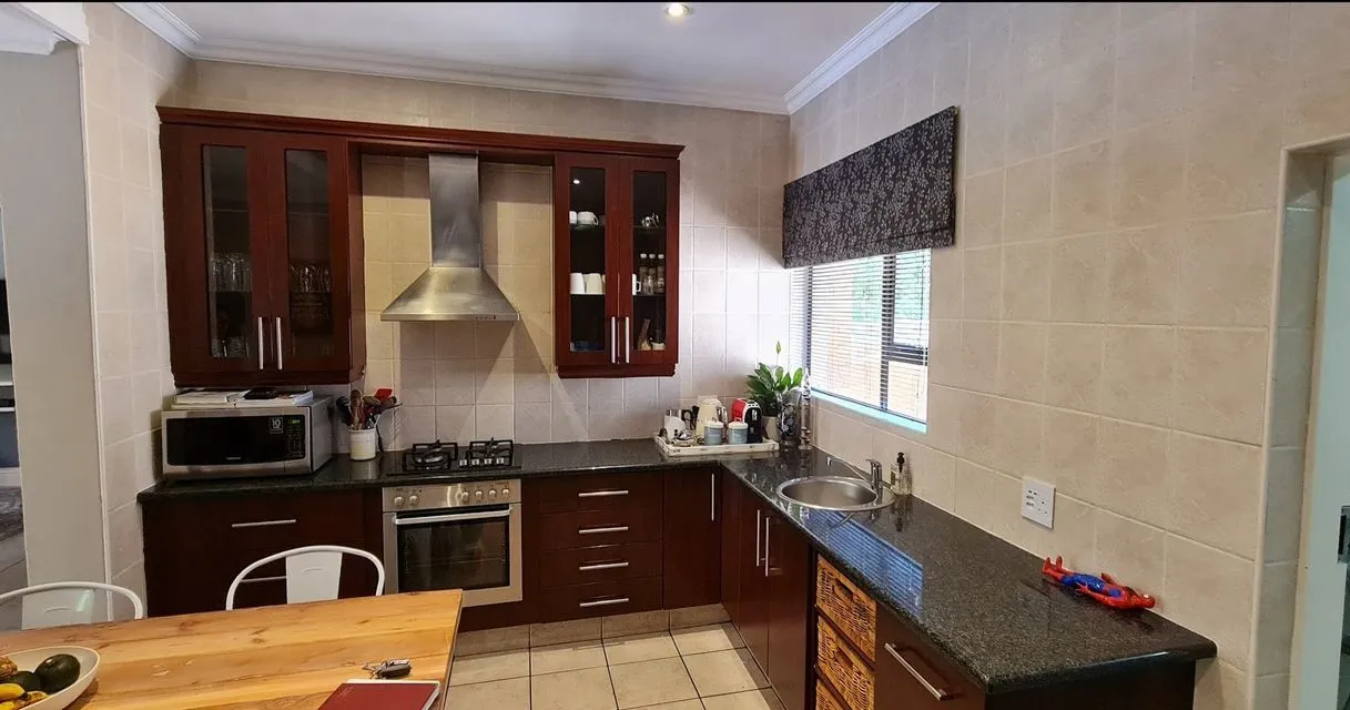 Before: a kitchen with dark mahogany-coloured cabinets, beige tiled walls, a steel extractor hood and dark granite countertops.