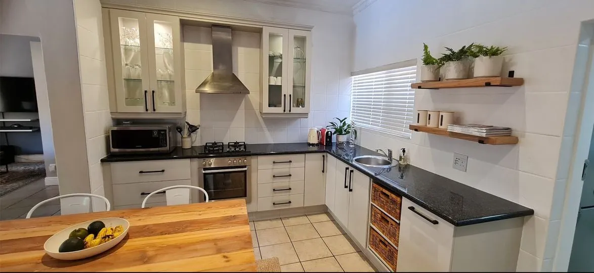 After: the kitchen with cream cabinets and black handles, white walls and two timber shelves holding potted plants.