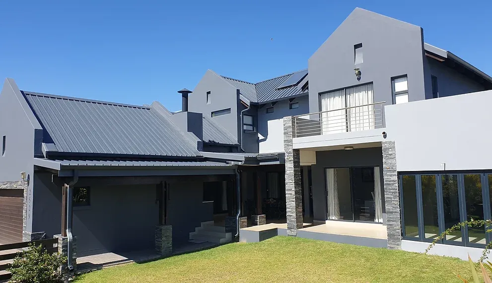 After: the same house painted in light and charcoal grey, with its dark roof and stone columns above a green lawn.