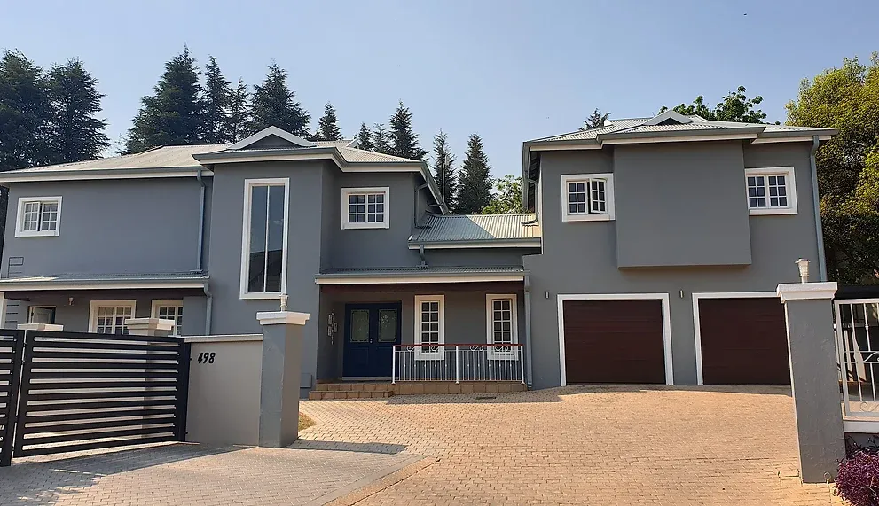 After: the house in mid grey with white window and garage surrounds and timber-toned garage doors, seen across the paved driveway.