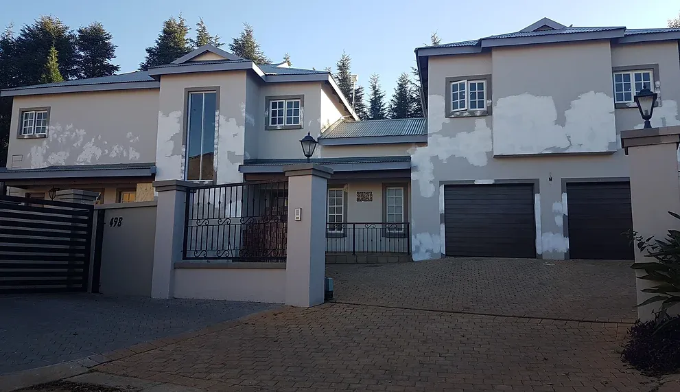 Before: a double-storey house with taupe walls covered in white repair patches, dark garage doors and a brick-paved driveway.