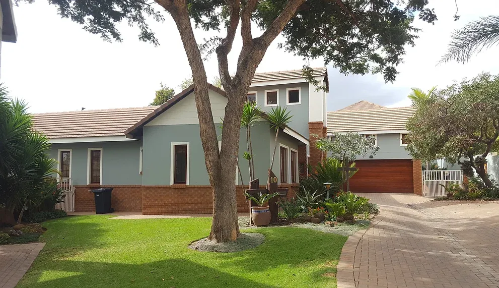 After: the house in soft grey-green with a pale gable, face-brick base and timber garage door, seen across the lawn.