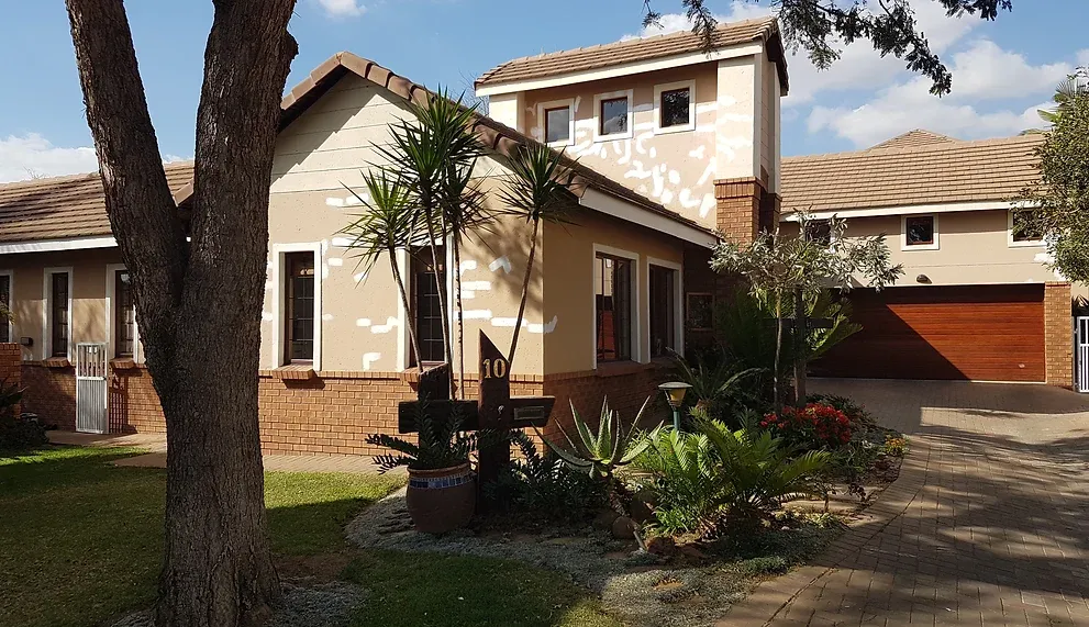 Before: a house with peach plaster walls dotted with pale repair patches above a face-brick base, behind a large tree and a garden bed.