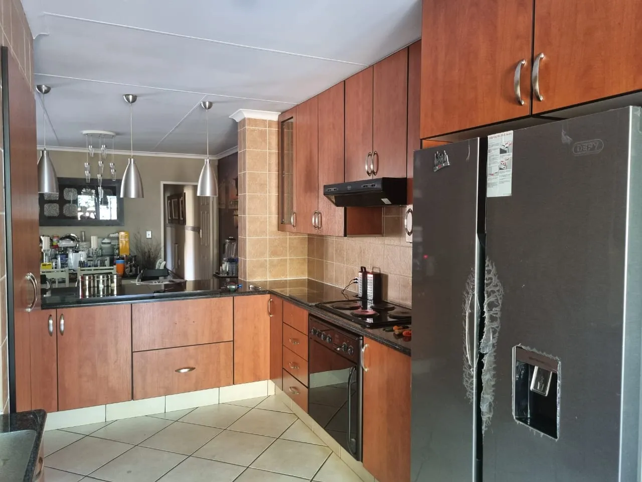 Before: a kitchen with cherry-brown cabinets, beige wall tiles, black countertops and three steel pendant lights.