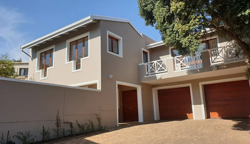 After: the house in warm taupe with white window surrounds and balustrades, beside two timber garage doors.