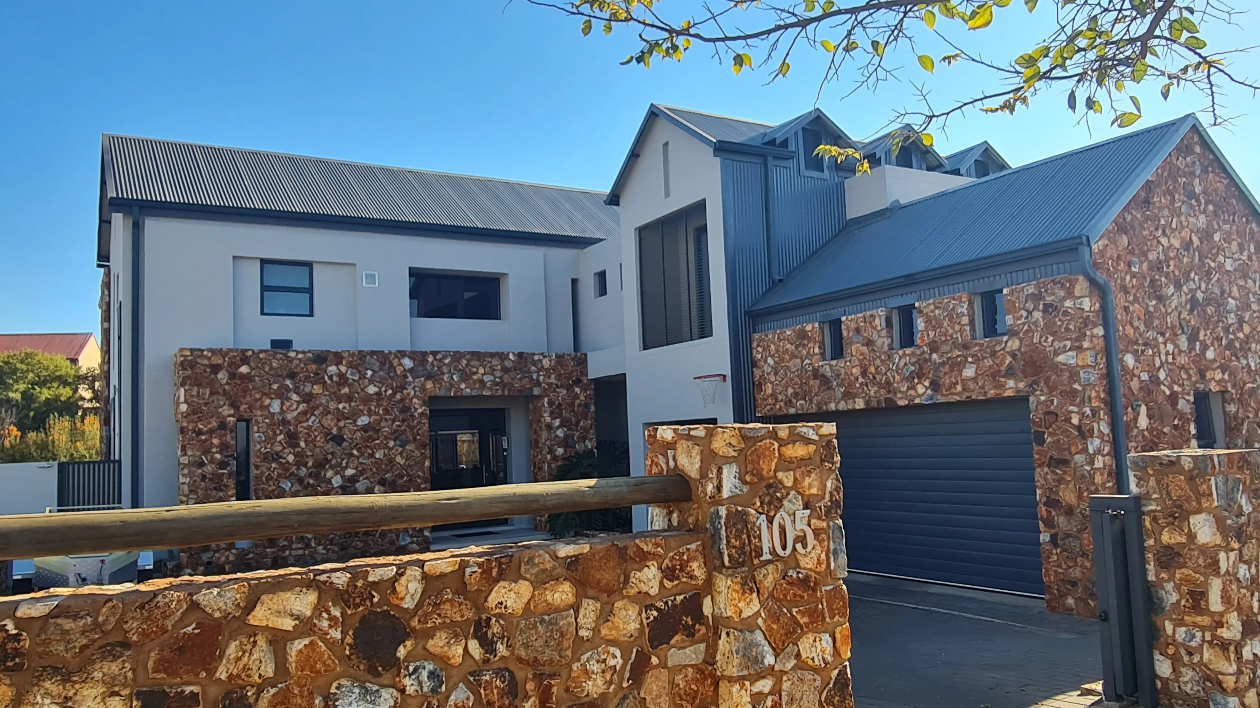 After: the same house with smooth cream plaster between the stonework and a closed charcoal garage door, seen over a stone boundary wall.