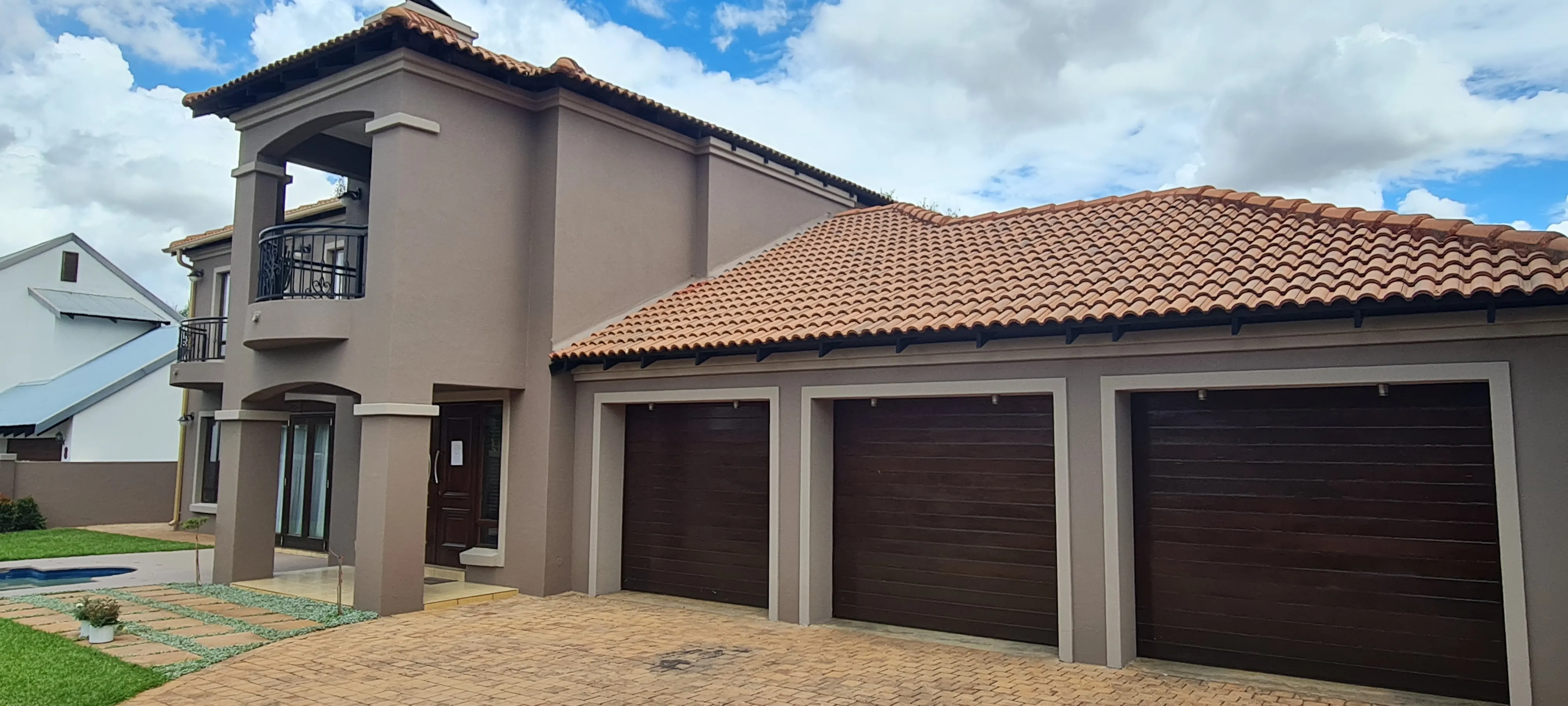 After: the house in warm taupe with paler surrounds framing the three garage doors and the entrance columns.