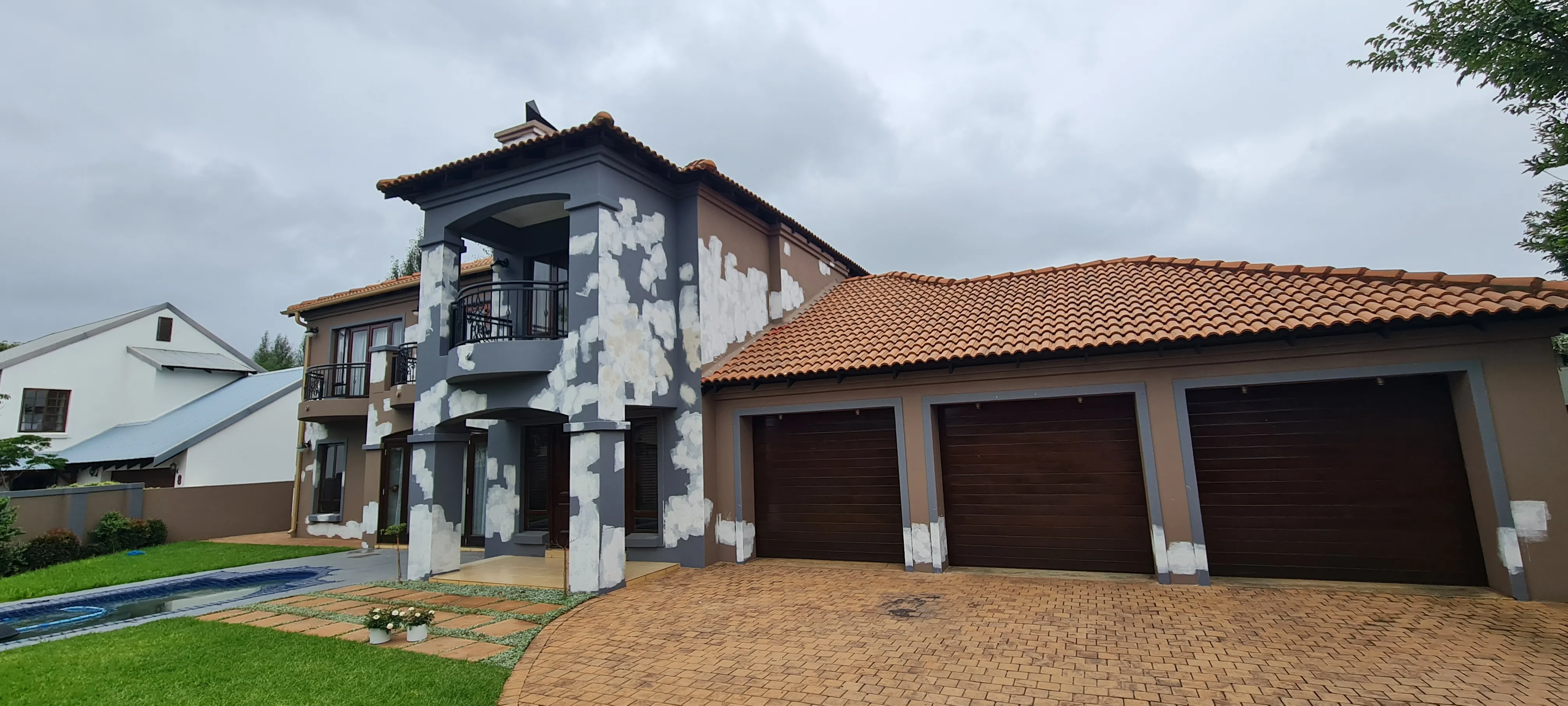 Before: a double-storey house with a terracotta tiled roof, its brown and grey walls covered in white repair patches beside three timber garage doors.