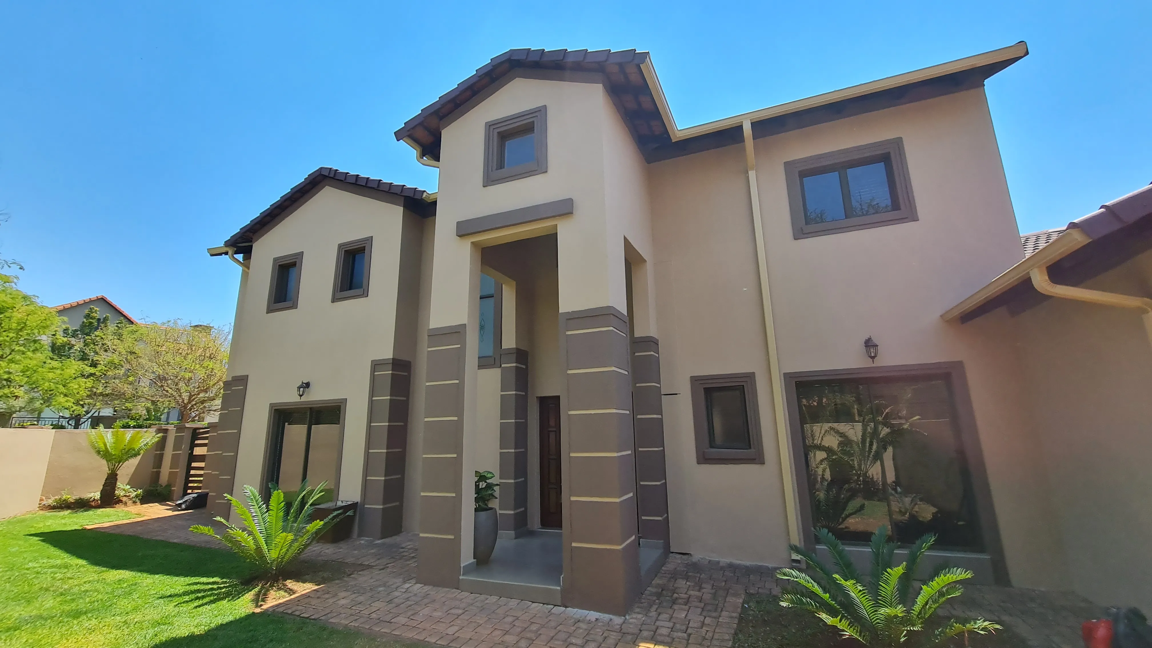After: the house with light cream walls, banded brown columns and brown window surrounds, with a neat lawn in front.