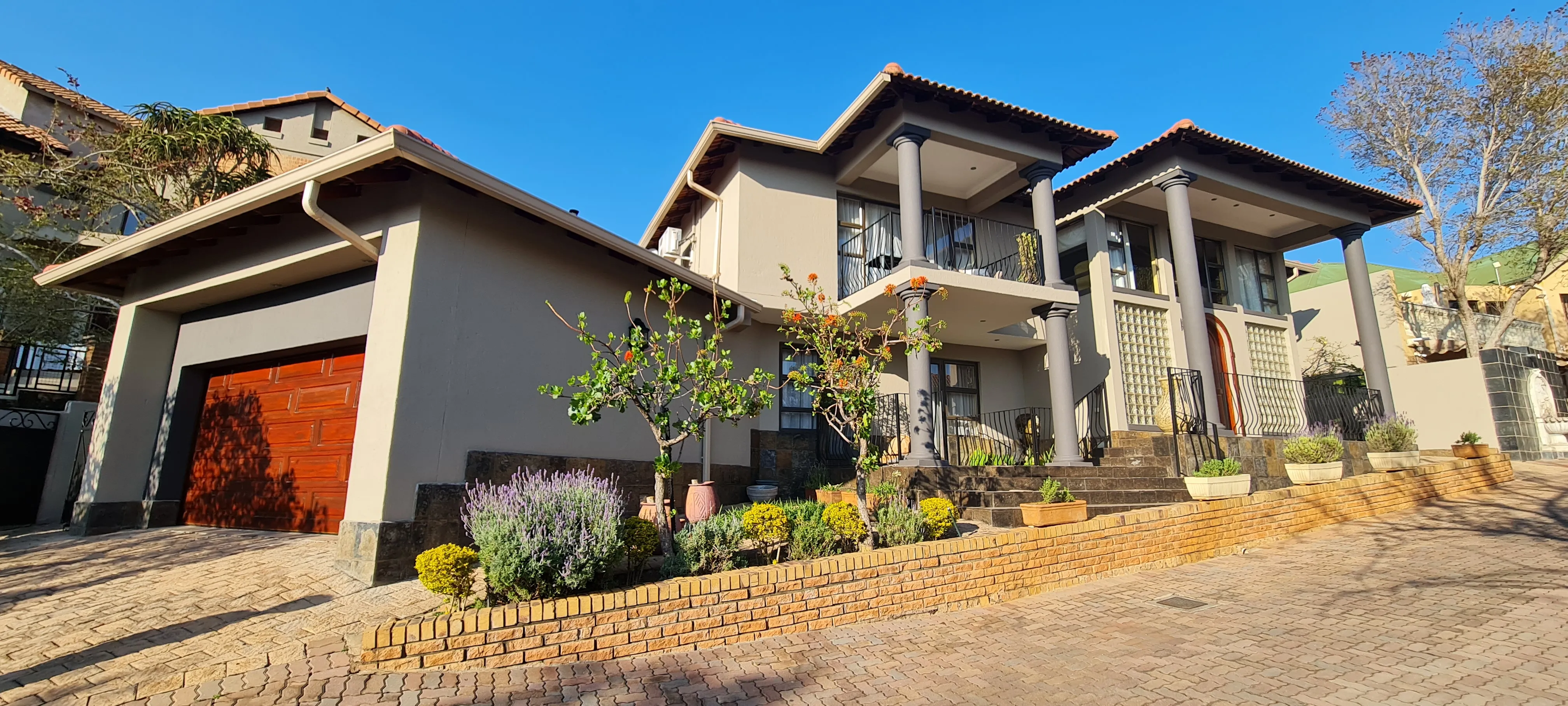 After: the house in grey with charcoal columns and garage surround, behind a planted brick border.