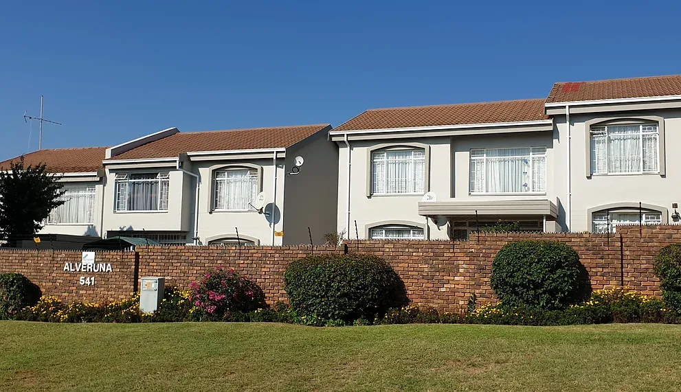 After: the townhouses in light grey with darker grey window surrounds, above the brick wall and a trimmed lawn.