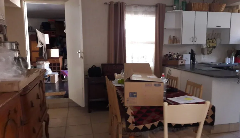 Before: a dining area with white walls, a table covered with a patterned cloth and a cardboard box, and white kitchen cabinets behind.