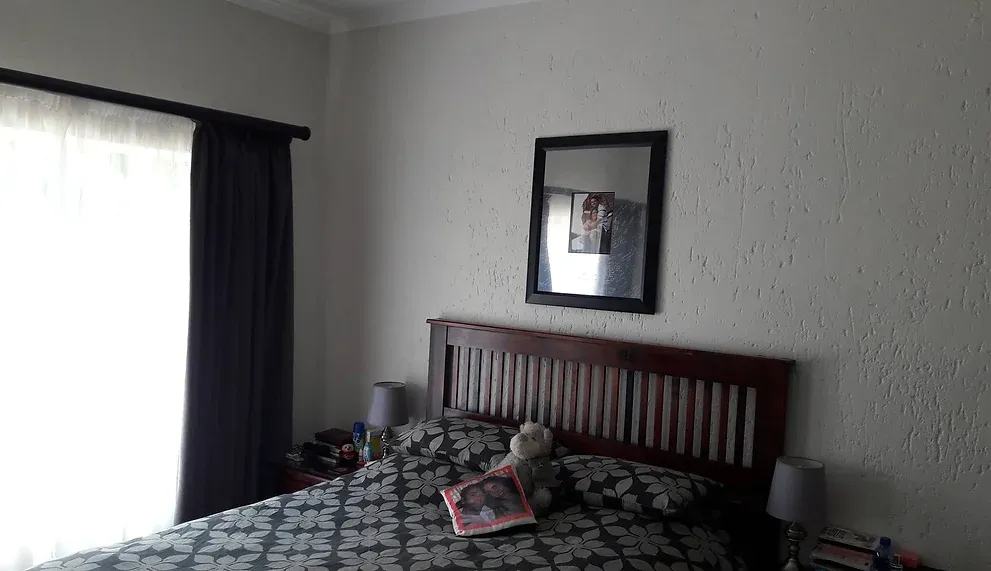 Before: a bedroom with pale textured walls, a dark timber slatted headboard and black-and-white floral bedding.