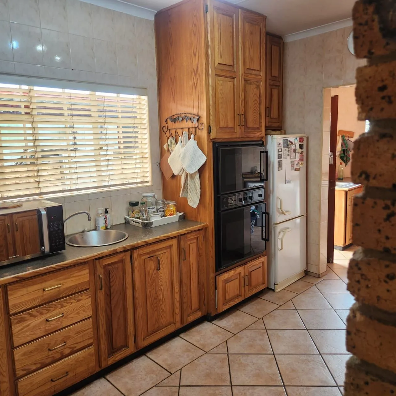 Before: oak cabinets and a built-in double oven beside a white fridge, with a doorway through to the scullery.