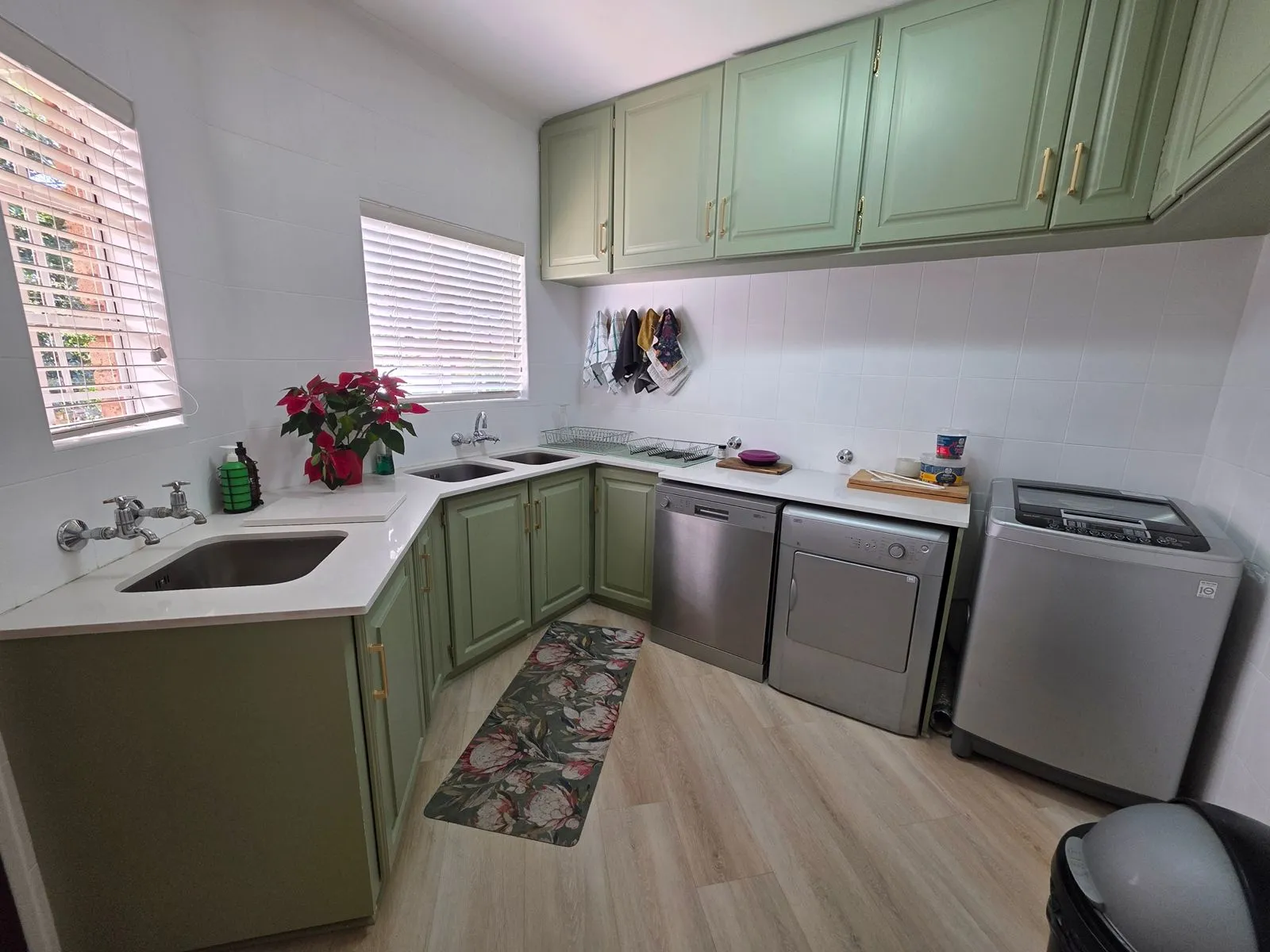 After: the scullery with sage green cabinets, white countertops, white wall tiles and a patterned runner on timber-look flooring.