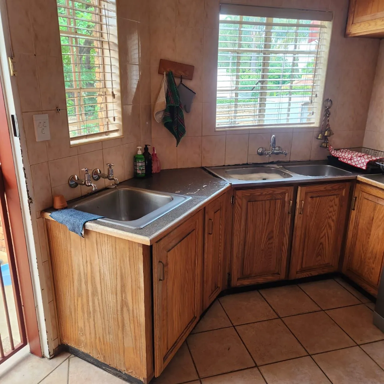 Before: a scullery with oak cabinets, dark countertops, two sinks and beige wall tiles.