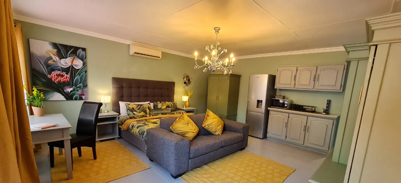 After: the suite with sage green walls, a green painted cupboard, mustard rugs and cushions, and a botanical painting above a desk.
