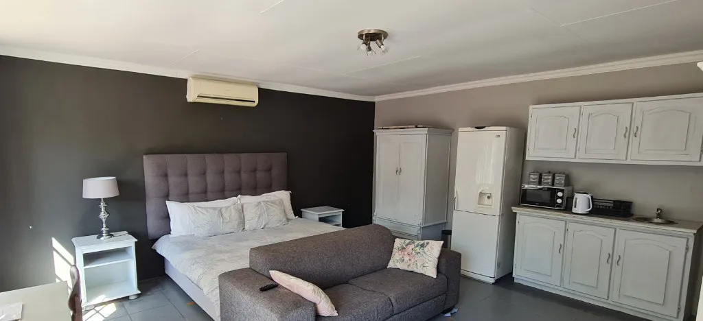 Before: a guest suite with a charcoal wall behind a grey upholstered bed, a grey sofa and a white kitchenette.