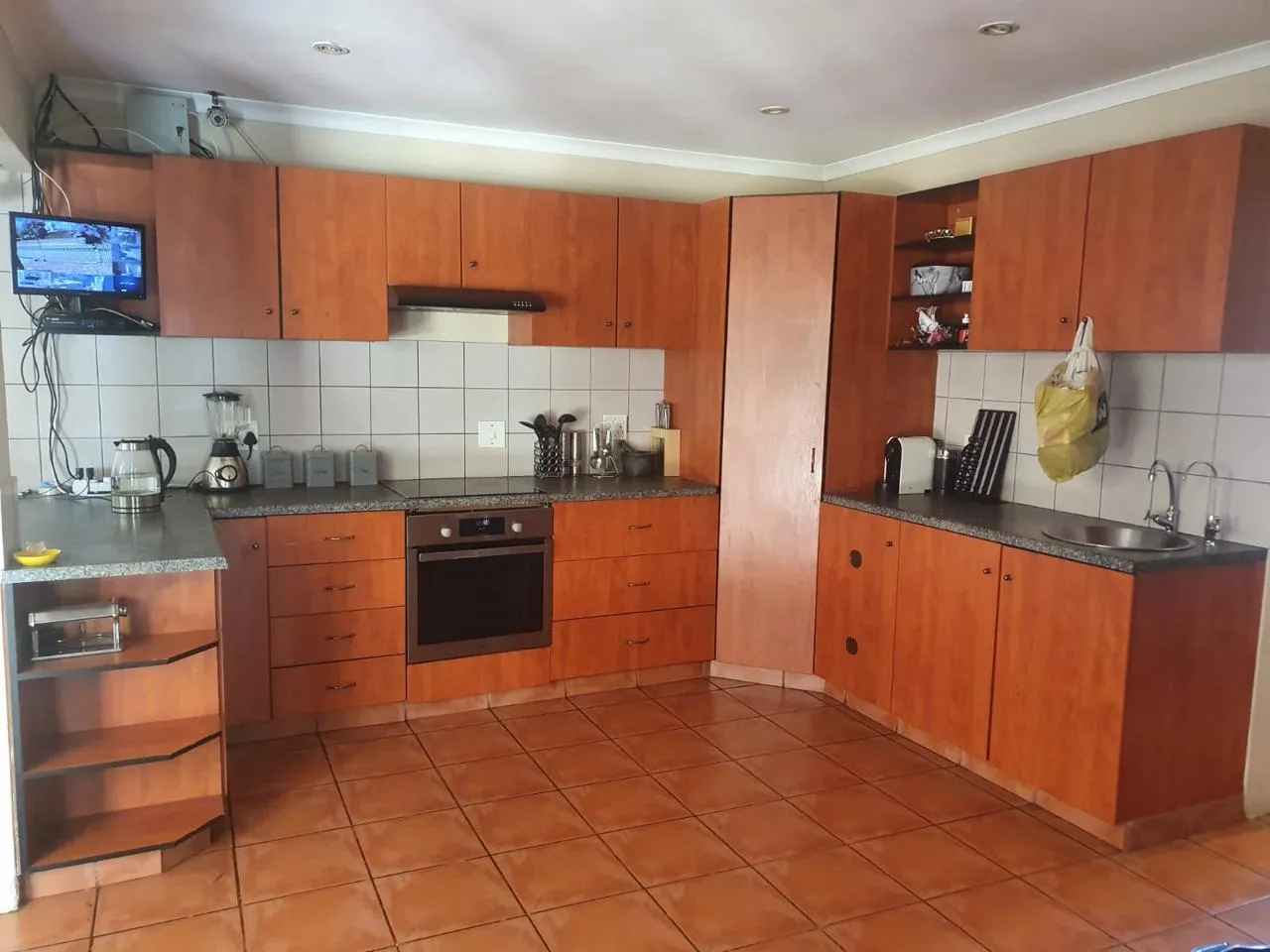 Before: a kitchen with cherry-toned cabinets, dark speckled countertops, white wall tiles and terracotta floor tiles.