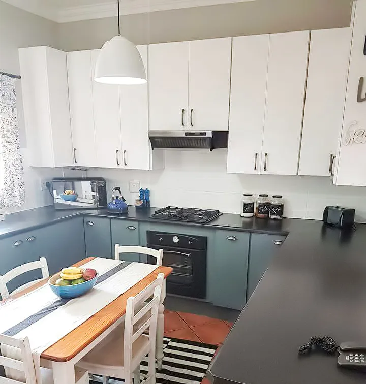 After: the kitchen with white upper cabinets, blue-grey lower cabinets, a white splashback and a black-and-white striped rug.